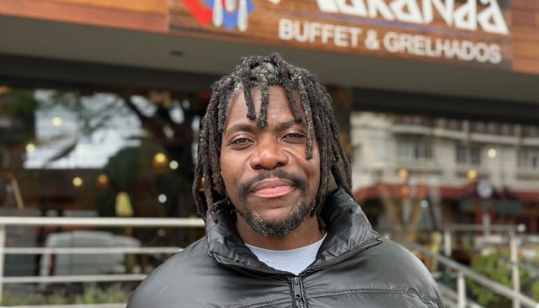 Um homem com dreadlocks e barba está parado em frente a um restaurante.