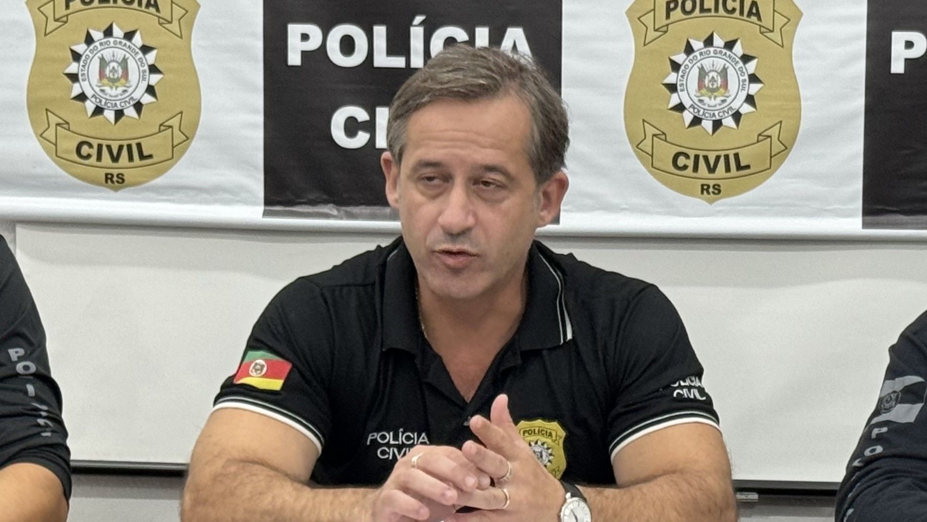 Um homem está sentado a uma mesa em frente a uma placa que diz polícia civil