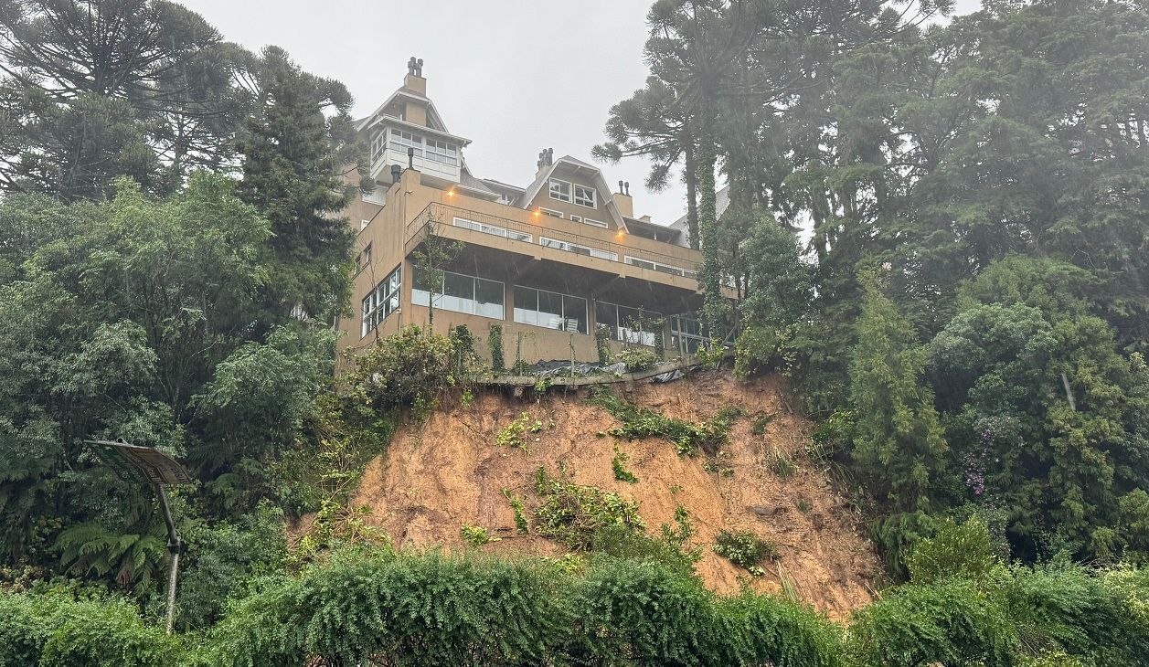 Uma grande casa está situada no topo de uma colina cercada por árvores.