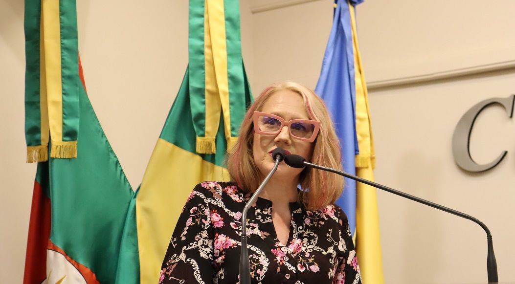 Uma mulher está falando ao microfone em frente às bandeiras.