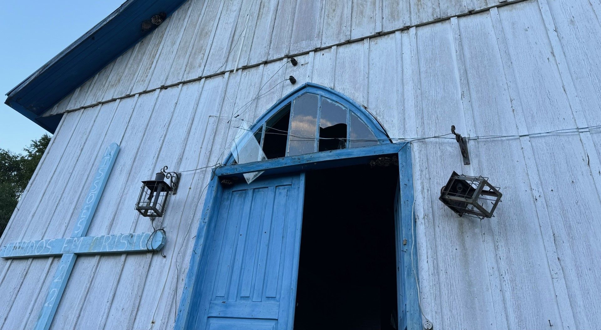 Uma igreja com porta azul e janela quebrada.