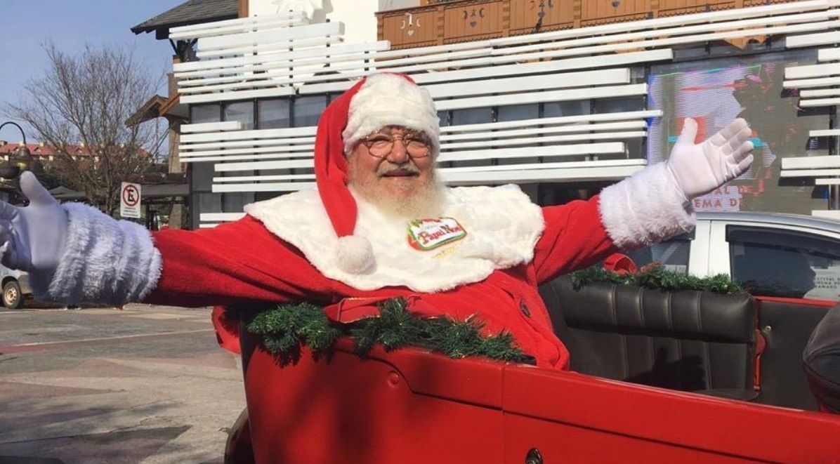 Um homem vestido de Papai Noel está parado em frente a um prédio com os braços estendidos.