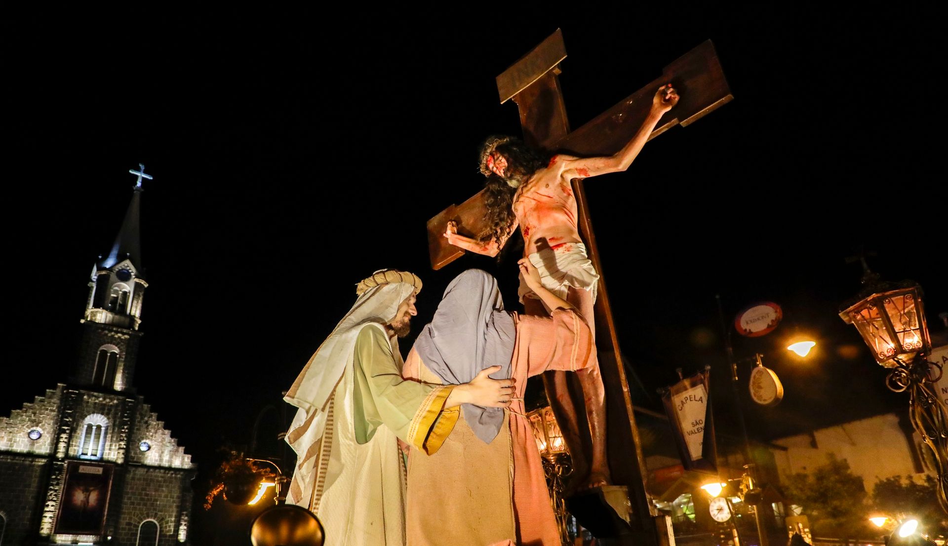 Uma estátua de Jesus pendurado em uma cruz com pessoas ao seu redor.