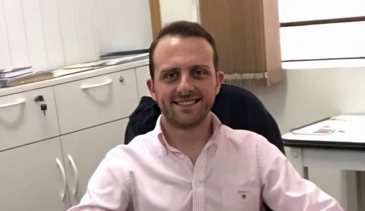 Um homem de camisa rosa está sentado em uma mesa e sorrindo.