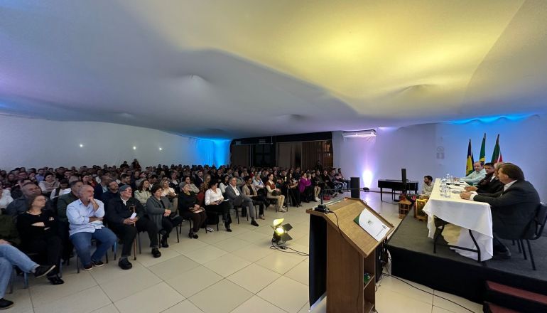 Um grande grupo de pessoas está sentado em uma sala em frente a um pódio.