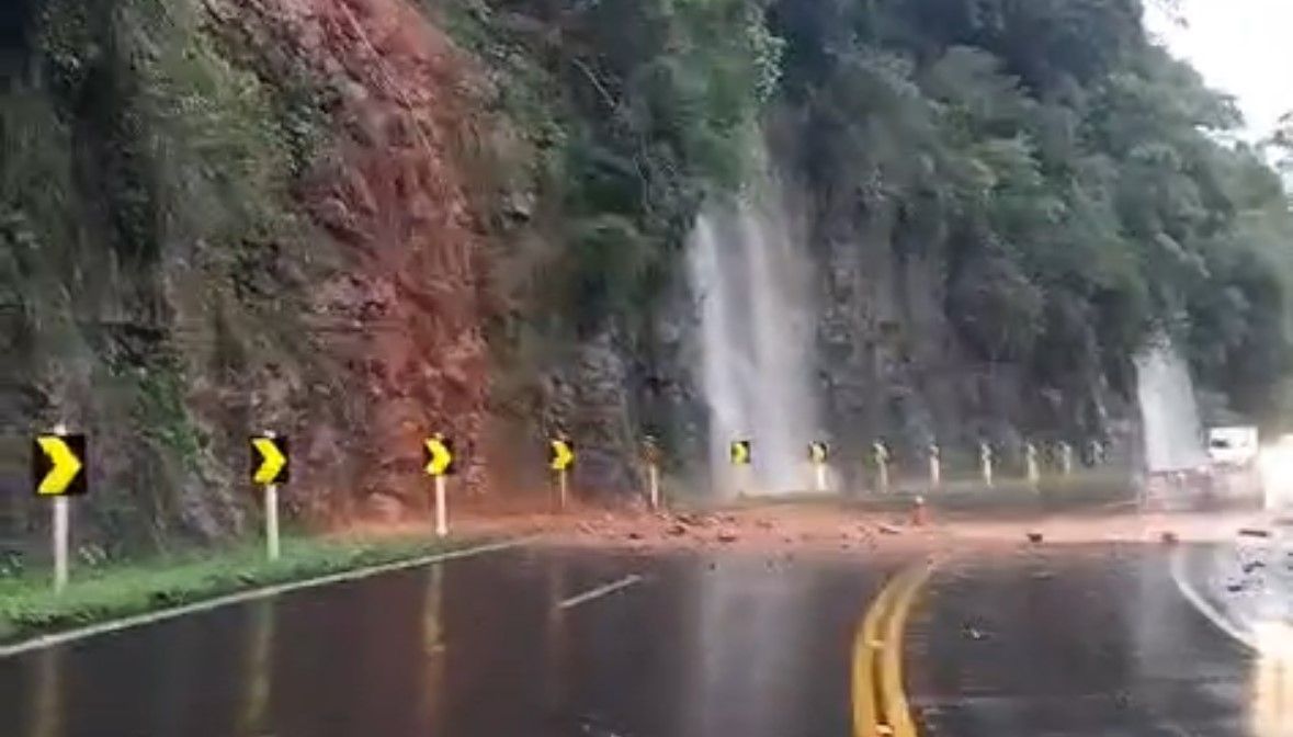 Um carro está dirigindo por uma estrada molhada próximo a uma parede de pedra.