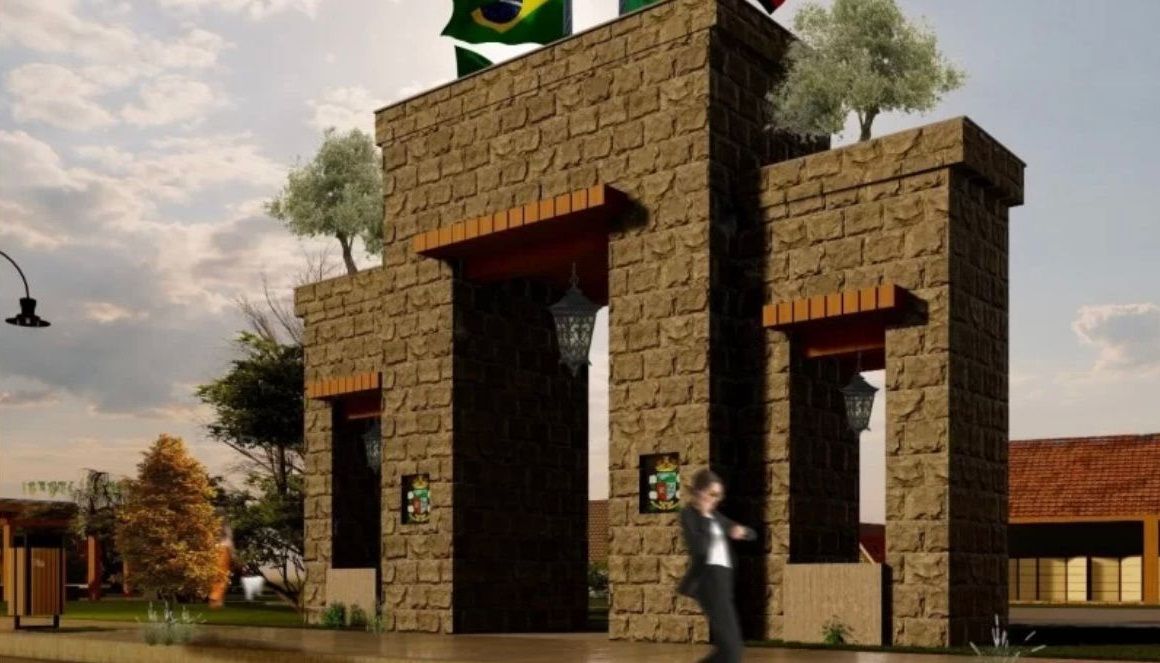Um homem caminha em frente a um arco de pedra com uma bandeira brasileira no topo.