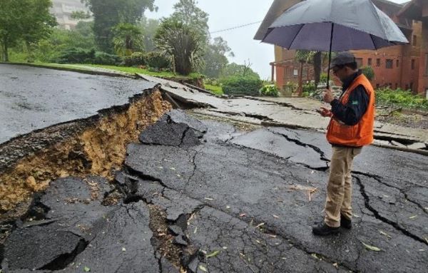 Um homem segurando um guarda-chuva fica ao lado de uma estrada rachada