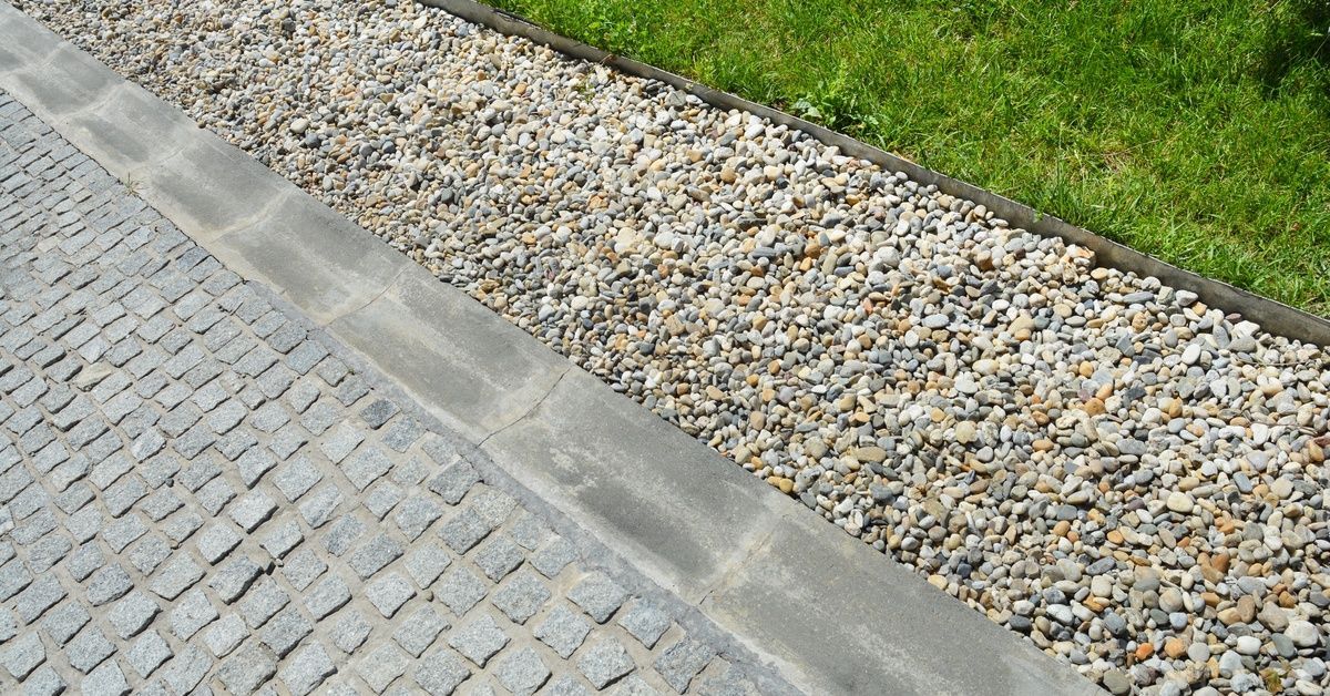 A modern drainage system featuring permeable gravel along cobblestone pavement and grass next to it.