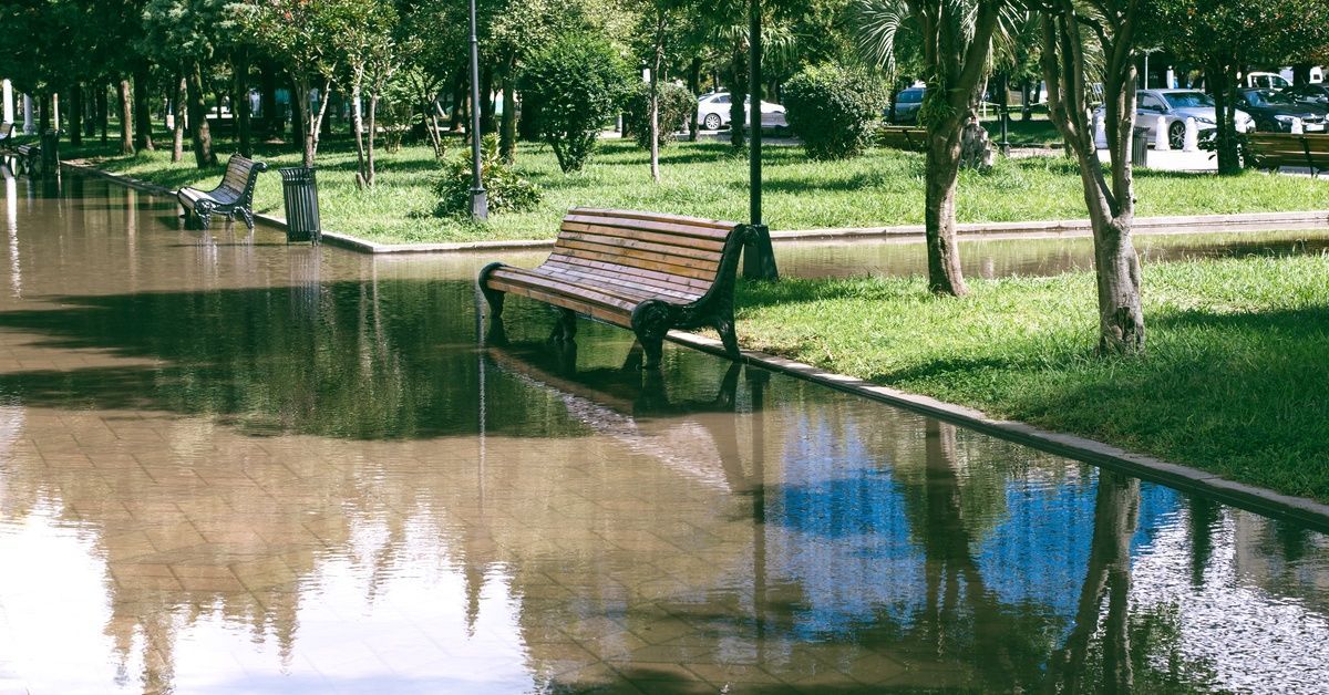 A boulevard park is flooded after heavy rain, covering all the pavement in the area.