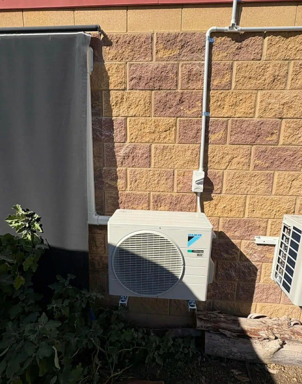 An Outdoor Air Conditioning Unit Mounted on a Brick Wall — BNS Refrigeration Services in Healy, QLD