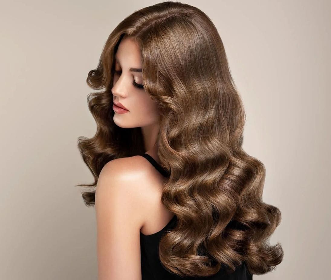 A Woman With Long Wavy Brown Hair is Wearing a Black Tank Top — Sophisticut Hair Salon in Mysterton, QLD