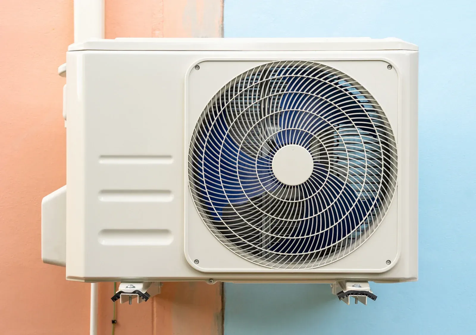 Outdoor air conditioning unit mounted on a wall, with a large blue fan and white casing