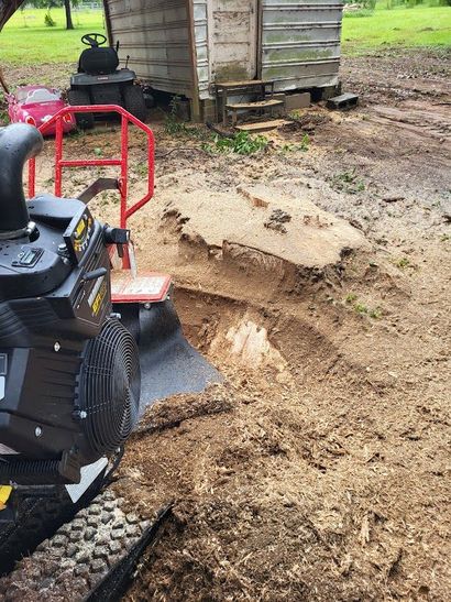 Red lawn tractor beside a dug-out dirt patch near a wooden shed in a muddy yard