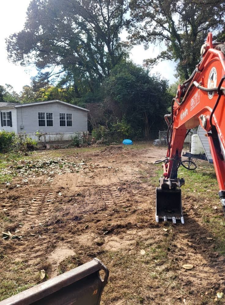 Orange excavator at a dirt lot beside a small house and trees