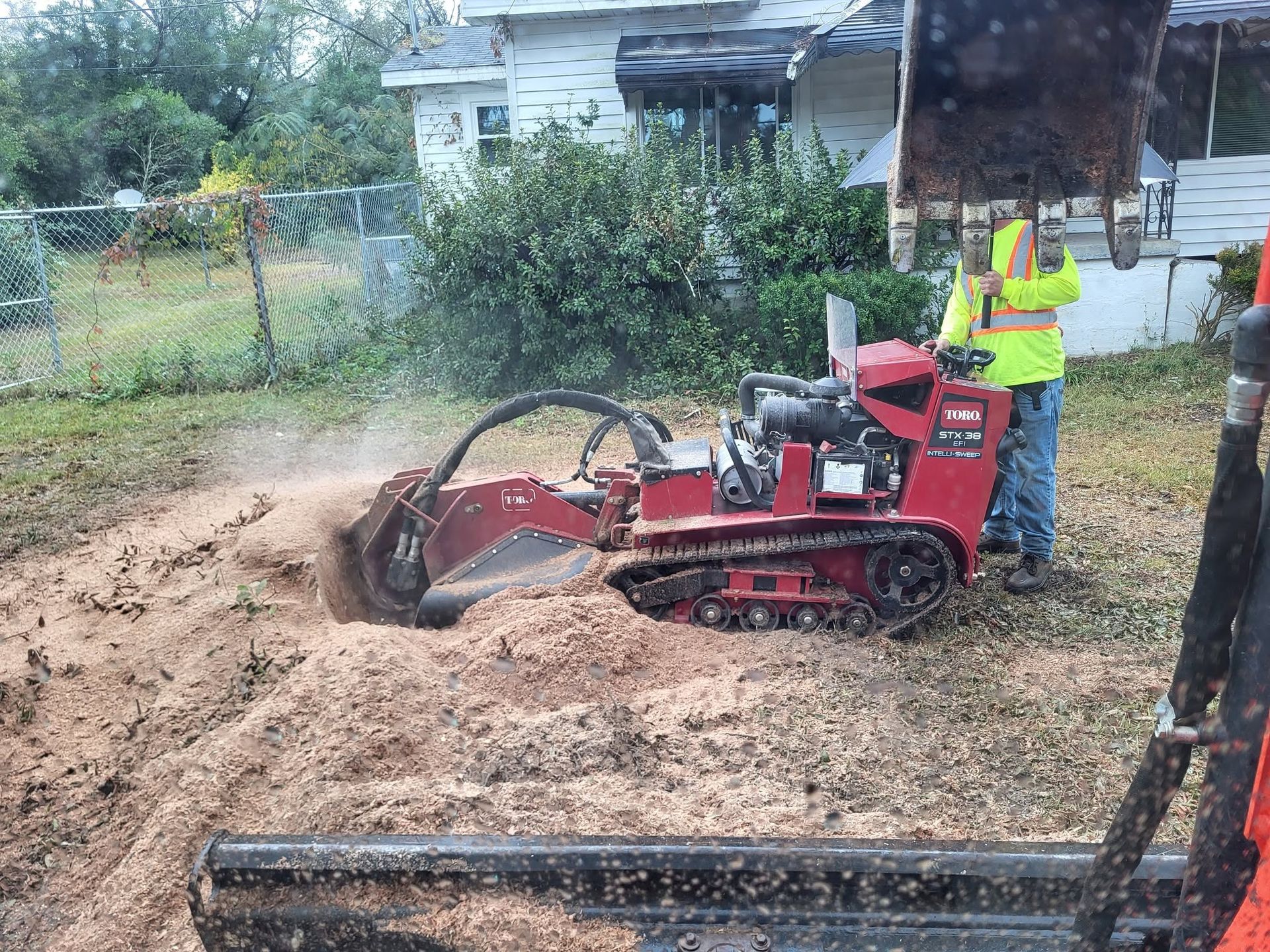Worker operating red skid steer digging dirt in a yard near a house
