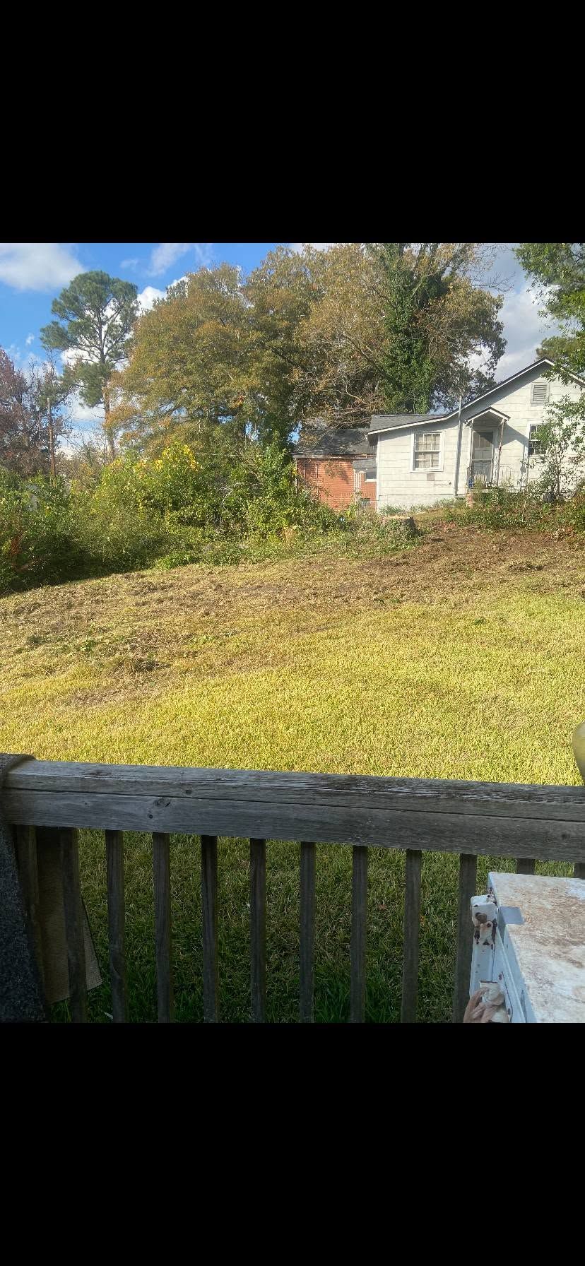 Backyard view with green lawn, trees, a house in the distance, and a wooden deck railing in front.