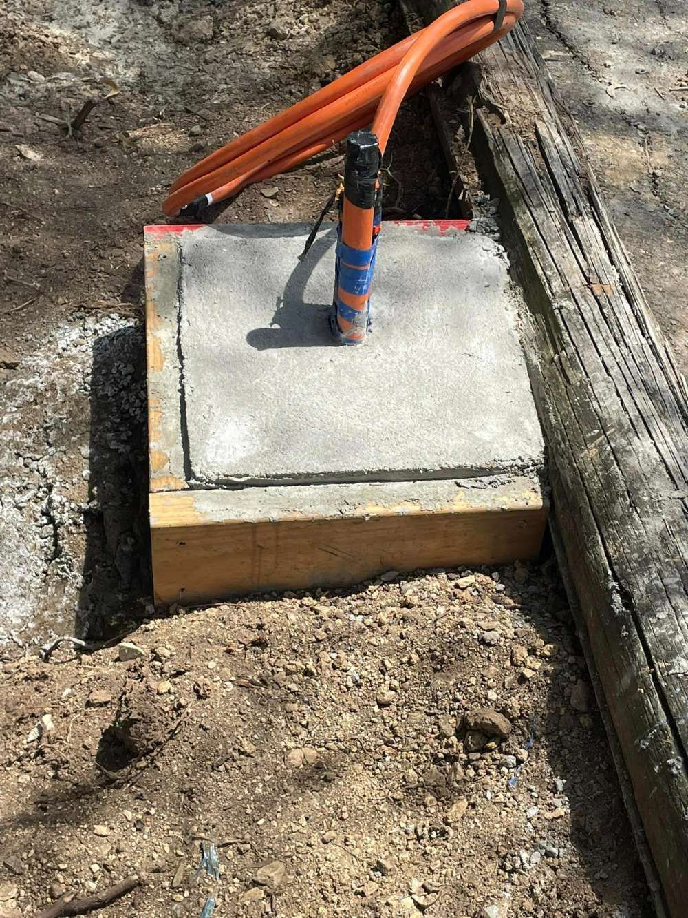 A Concrete Block Is Sitting On Top Of A Dirt Ground Next To A Wooden Post — BayCoast Electrical & Control Solutions in Braidwood, NSW