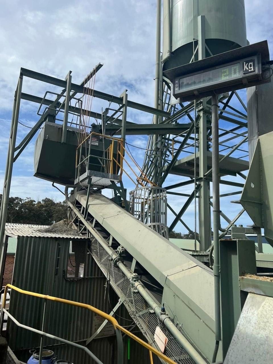 A Conveyor Belt In A Factory With A Silo In The Background — BayCoast Electrical & Control Solutions in Maloneys Beach, NSW