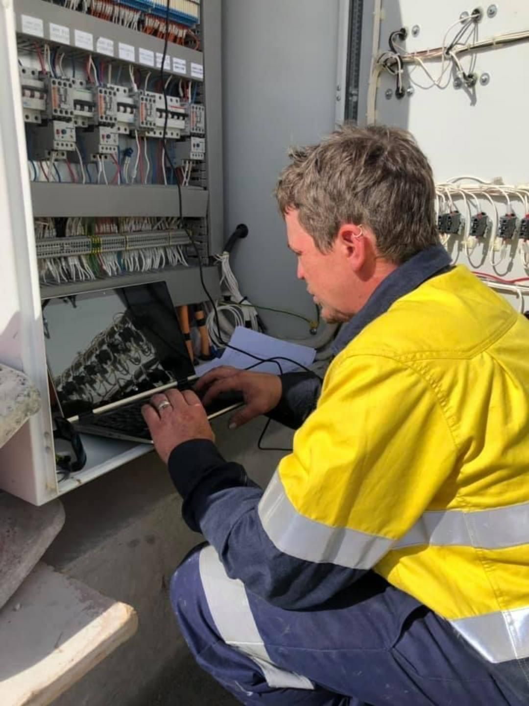 A Man In A Yellow Jacket Is Working On A Laptop — BayCoast Electrical & Control Solutions in Maloneys Beach, NSW