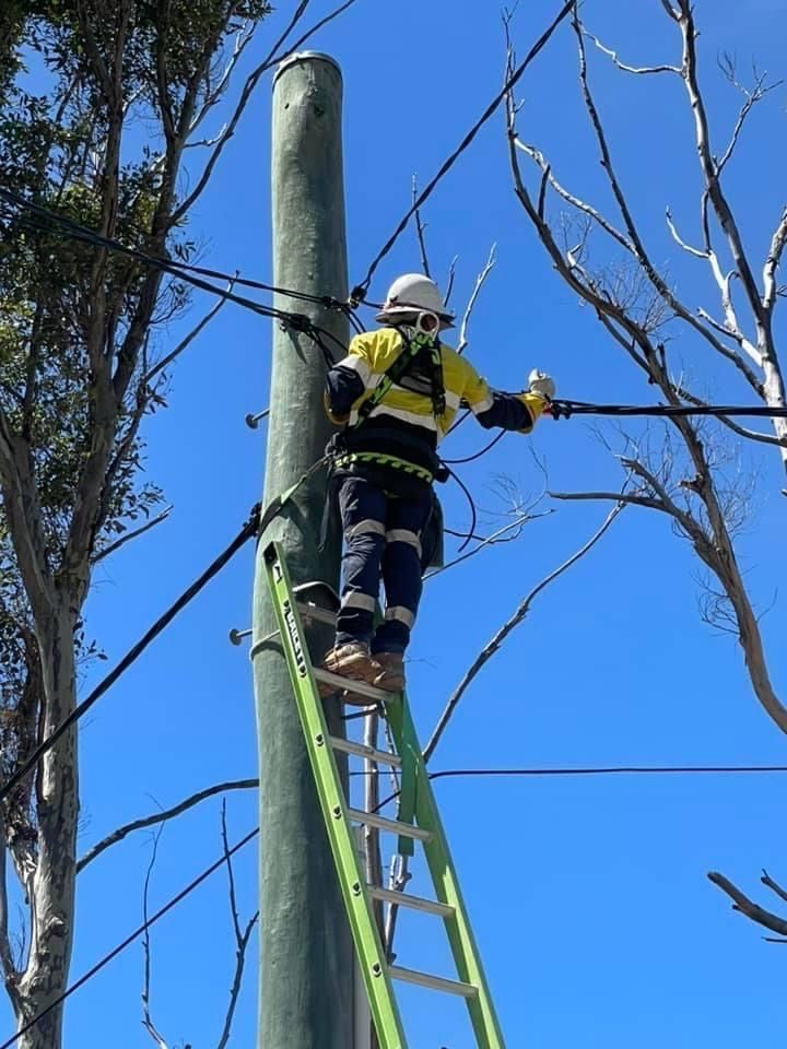 A Man Is Standing On A Ladder On Top Of A Power Pole — BayCoast Electrical & Control Solutions in Maloneys Beach, NSW