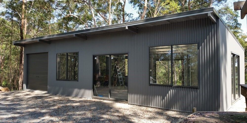 A Small House With A Lot Of Windows And A Garage Is Surrounded By Trees — BayCoast Electrical & Control Solutions in Ulladulla, NSW