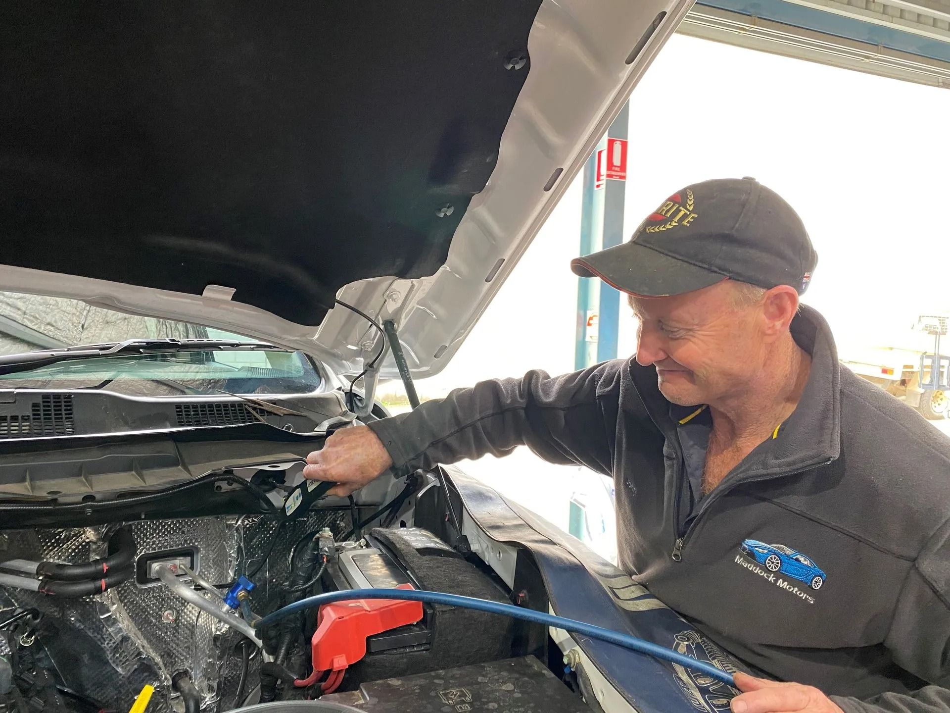 Mechanic inspecting an engine bay with the hood open, using a tool inside the car. — Maddock Motors-Wodonga Auto Air In Wodonga, VIC