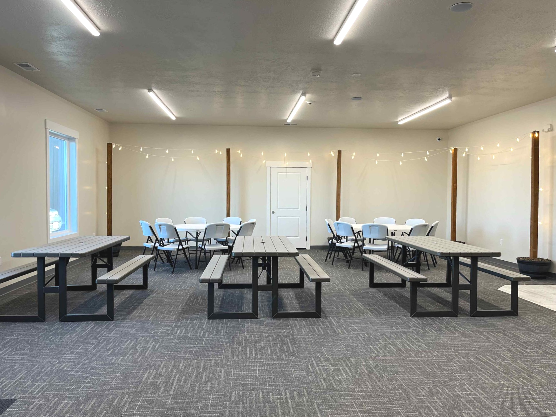 Empty room with tables, benches, and chairs, with fluorescent lights, and a door.