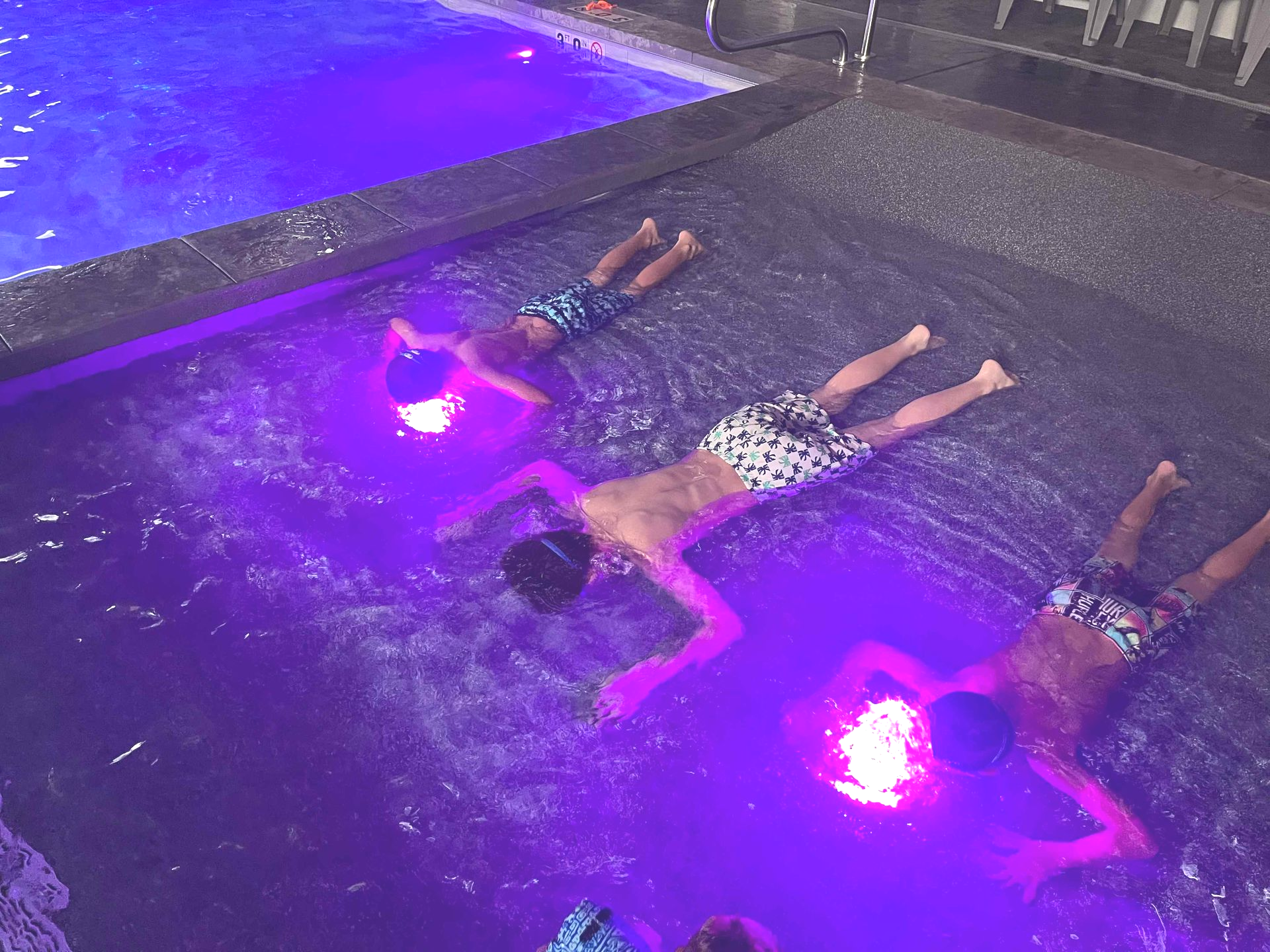 Three children floating in a shallow pool with purple lighting, each with a glowing orb.