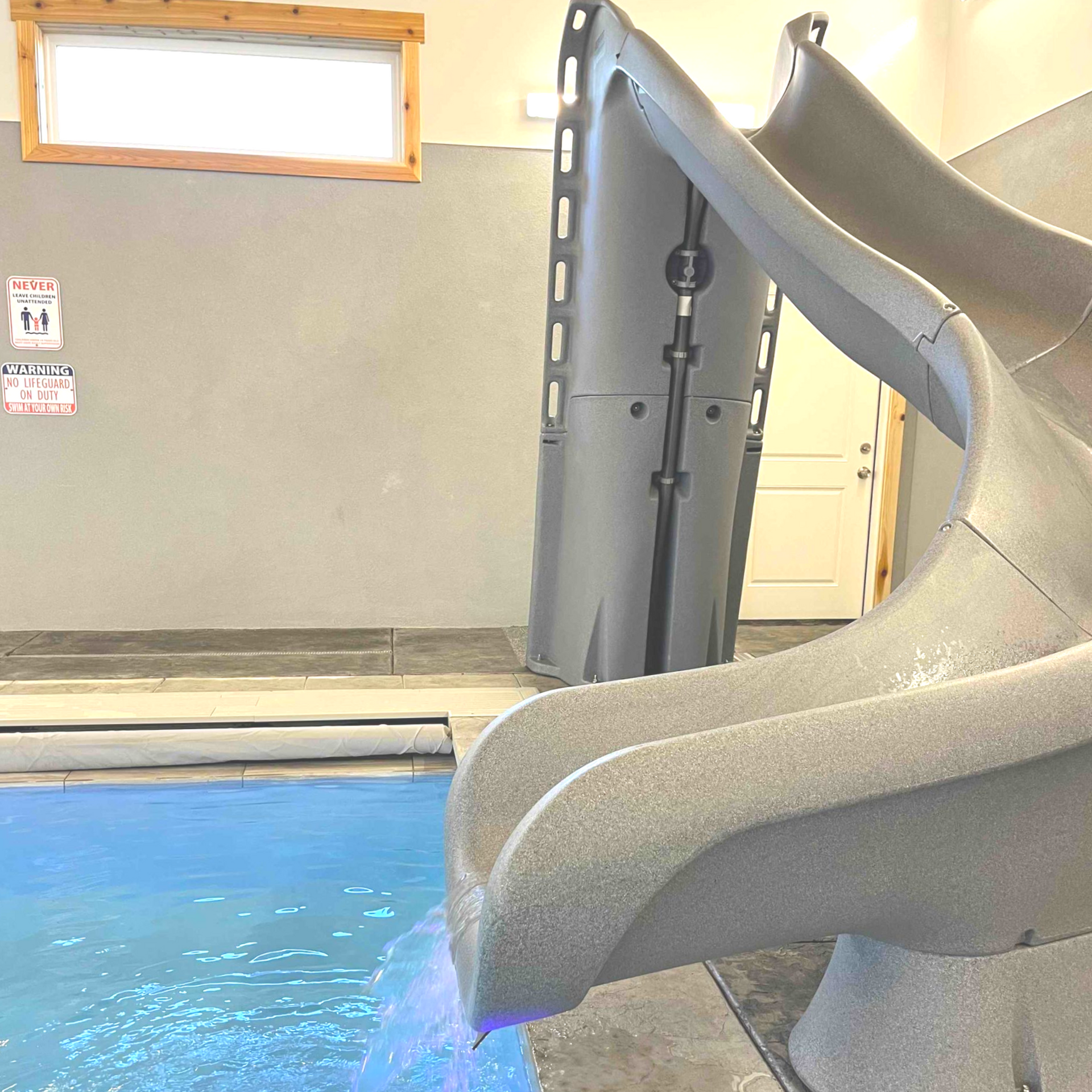 Indoor pool with a gray waterslide. Water splashes into the pool.