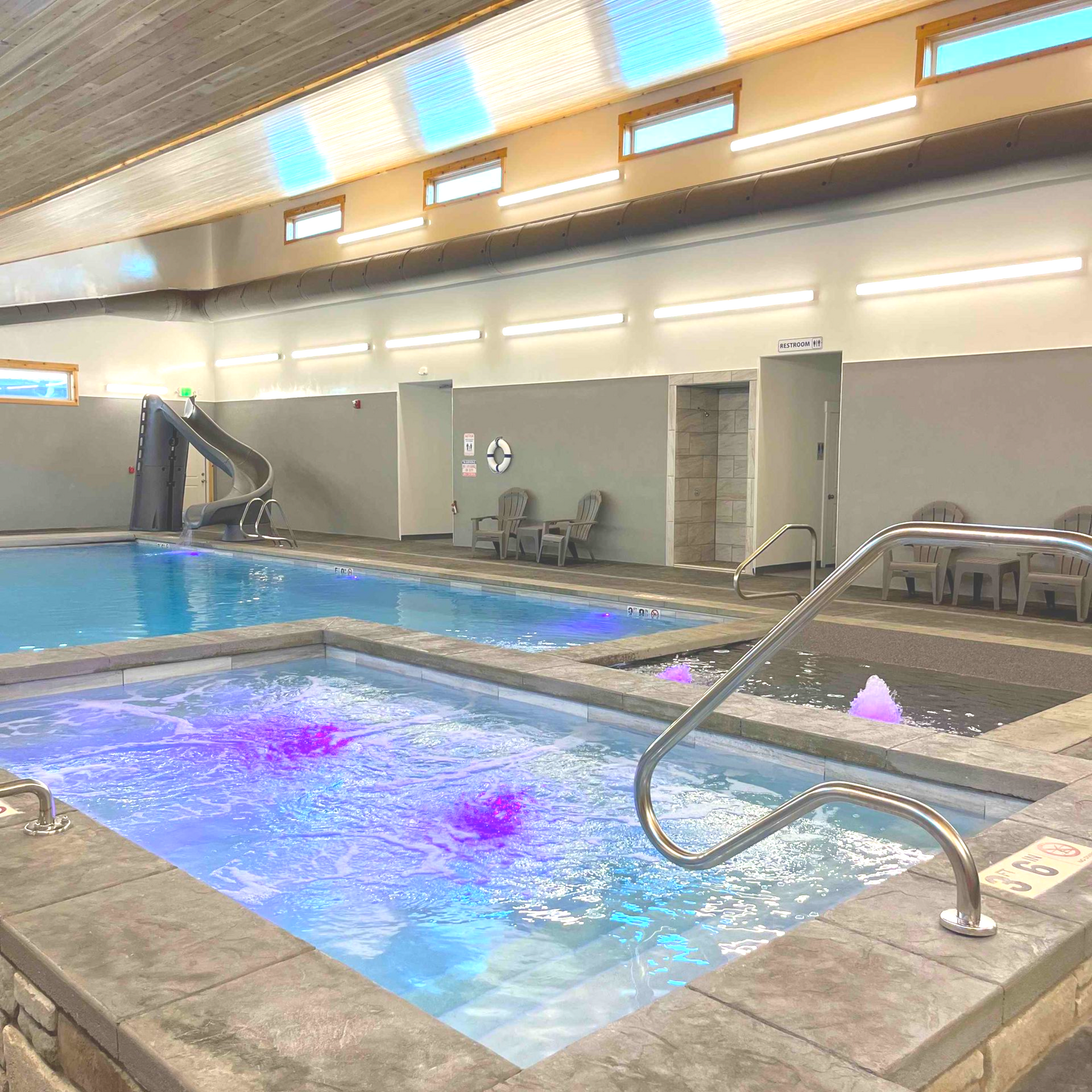 Indoor pool with a slide and jacuzzi, brightly lit with skylights.