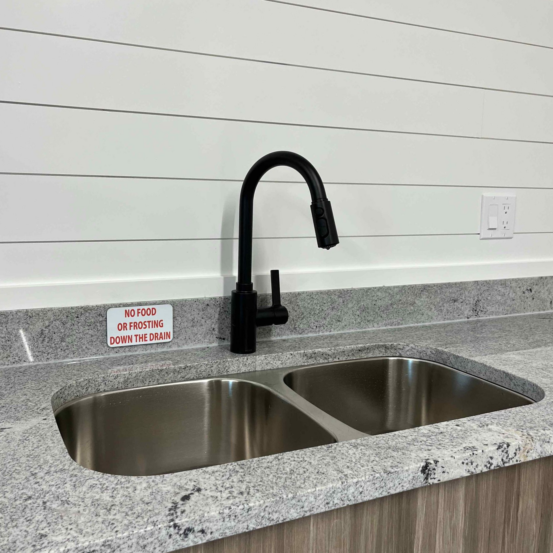 A kitchen sink with a black faucet on a speckled countertop against a white shiplap wall.