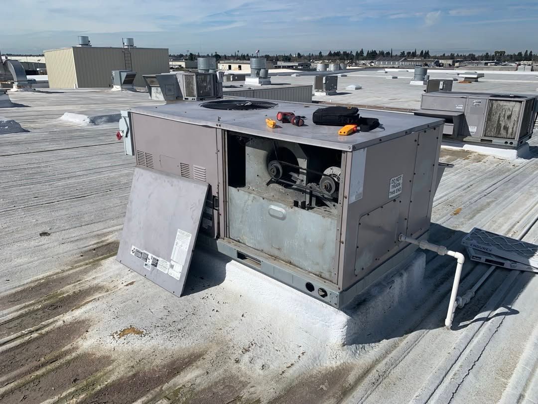 Damaged rooftop HVAC unit with an open panel and debris on a snowy roof.