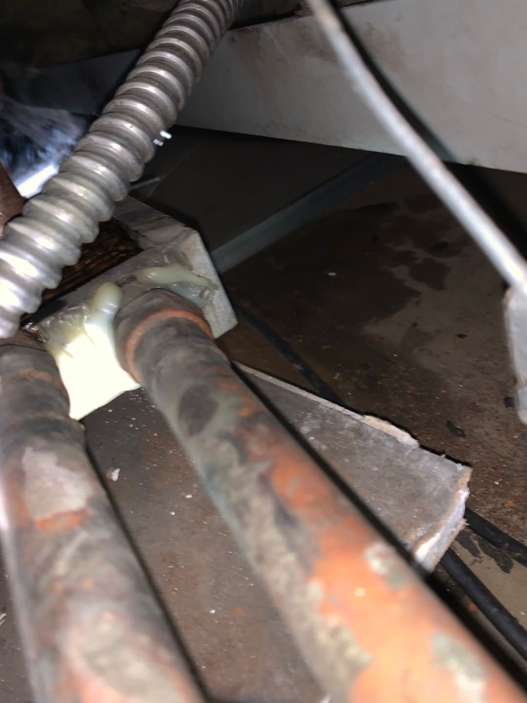 Close-up of rusty pipes and a cable inside a dark, cramped utility space