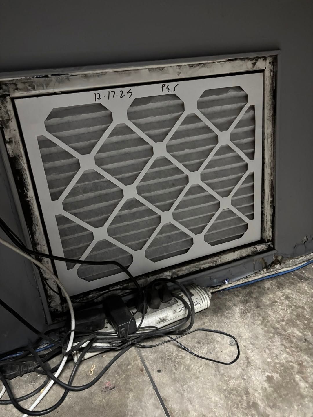 Dirty window AC unit with tangled cables on a concrete floor