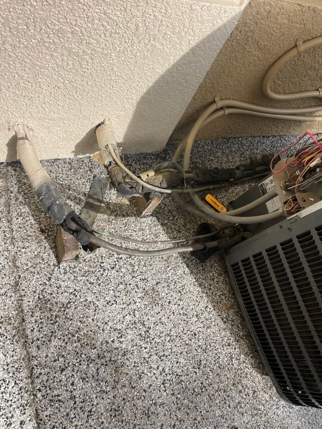 Exposed electrical wires and cables beside a wall and floor, next to a vented unit and a damaged patch of flooring.