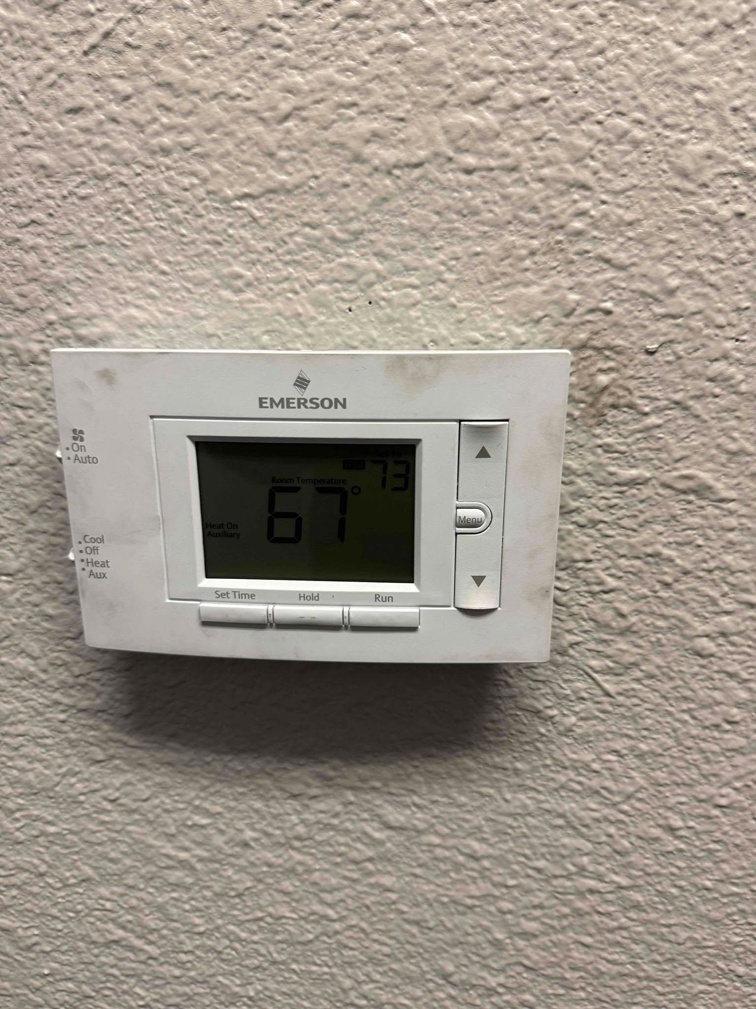 Wall-mounted digital thermostat on a beige textured wall showing 67°