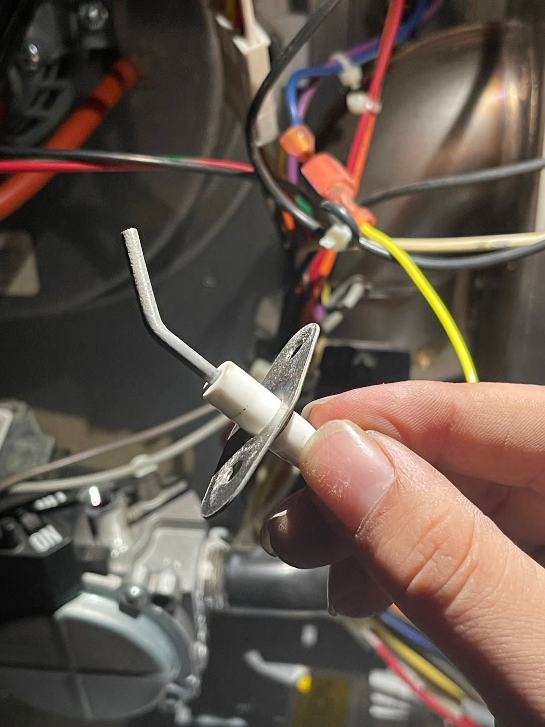 Close-up of a hand holding a small metal fastener with a white cable tie against an engine bay background