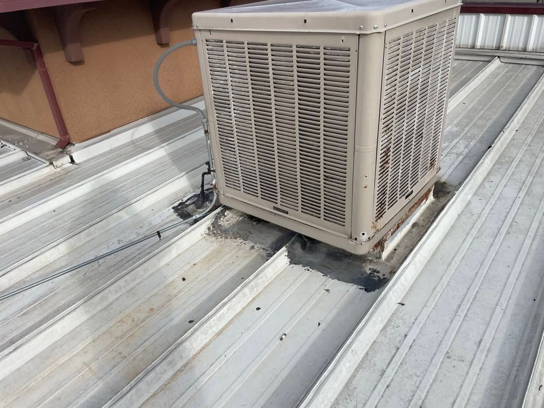 Rooftop HVAC unit beside a wall on a corrugated metal roof.