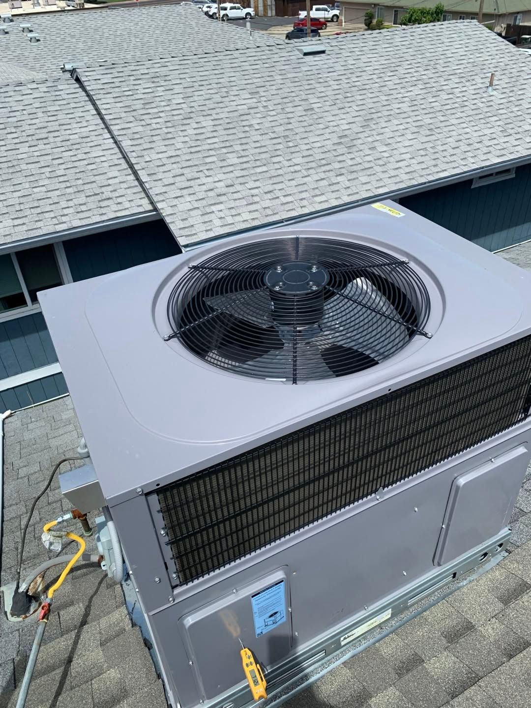 Rooftop HVAC unit with a large fan, mounted beside a shingled roof.