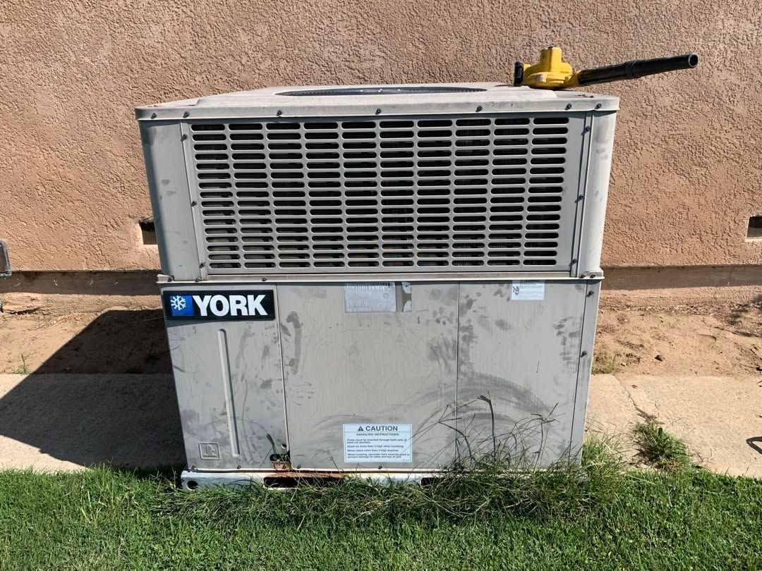 YORK outdoor HVAC unit with a yellow valve handle against a stucco wall on grass.