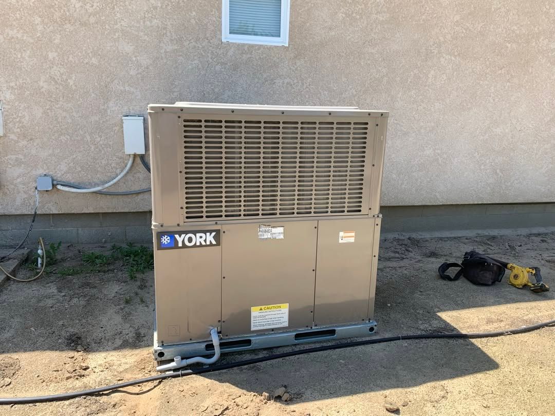 Outdoor York HVAC unit beside a stucco wall, with a yellow tool on the ground.