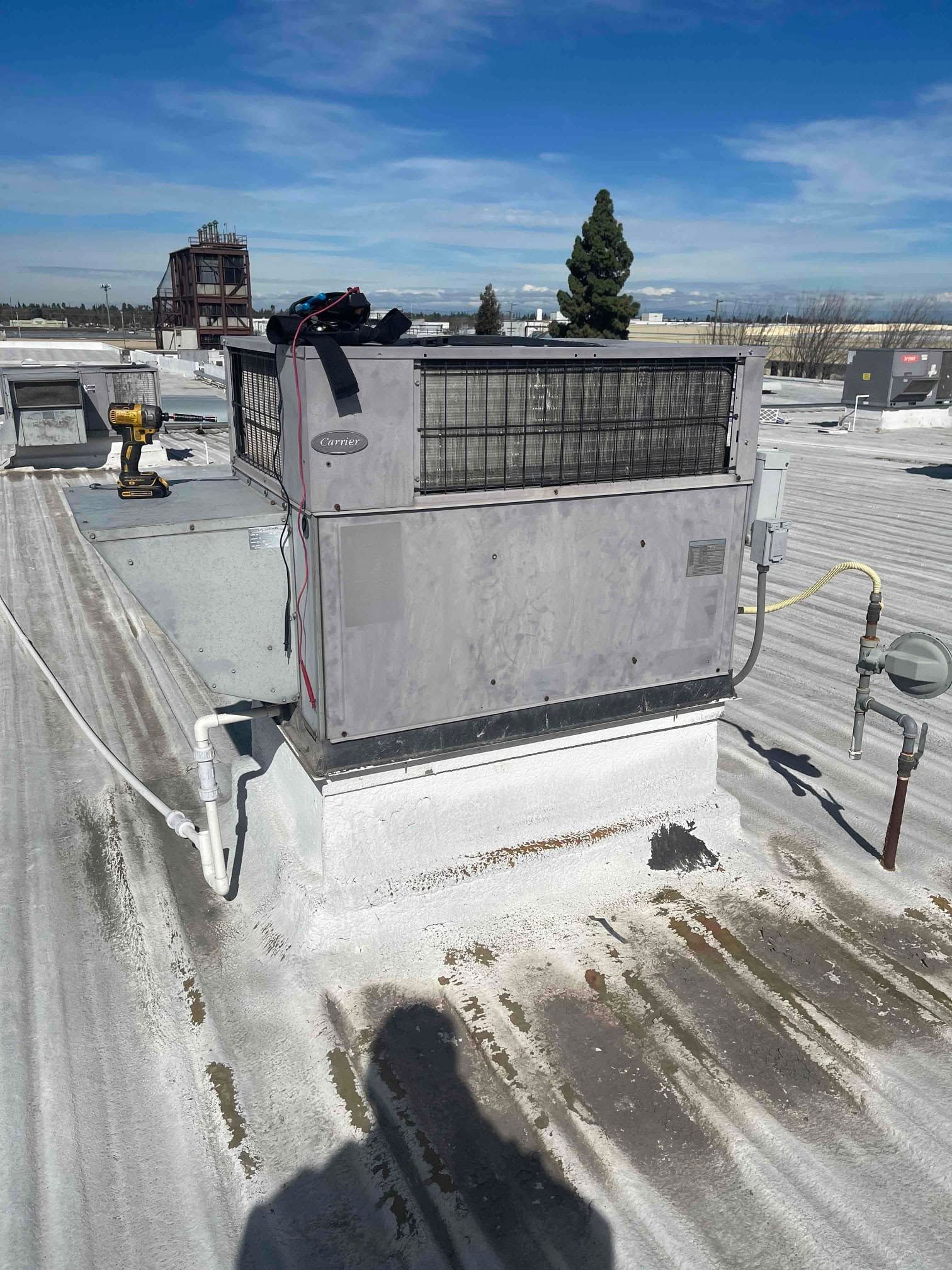 Snow-covered rooftop with a small vent structure and city skyline under a blue sky.