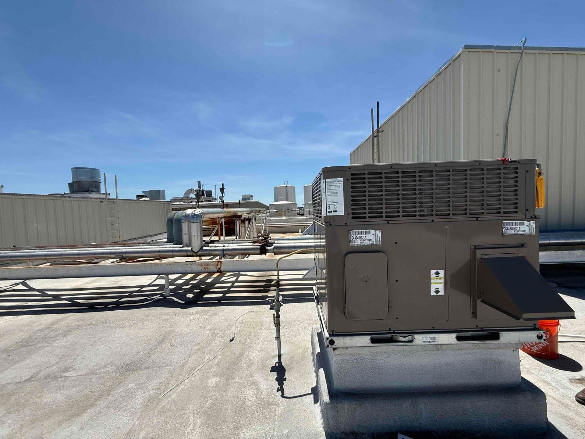 Rooftop HVAC unit beside pipes and ductwork under a clear blue sky.
