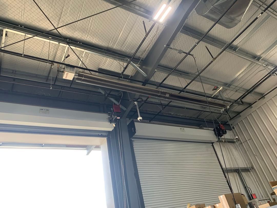 Industrial garage interior with open roll-up door, overhead tracks, and exposed ceiling beams