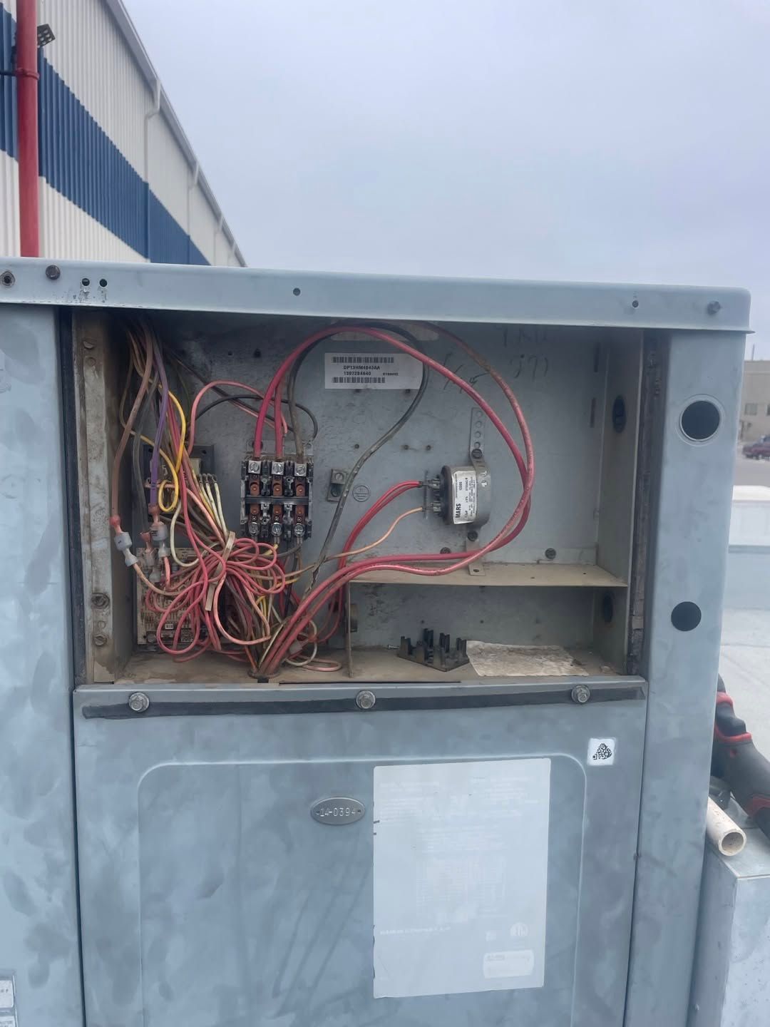 Open electrical control box with exposed wires and components on an outdoor metal unit.