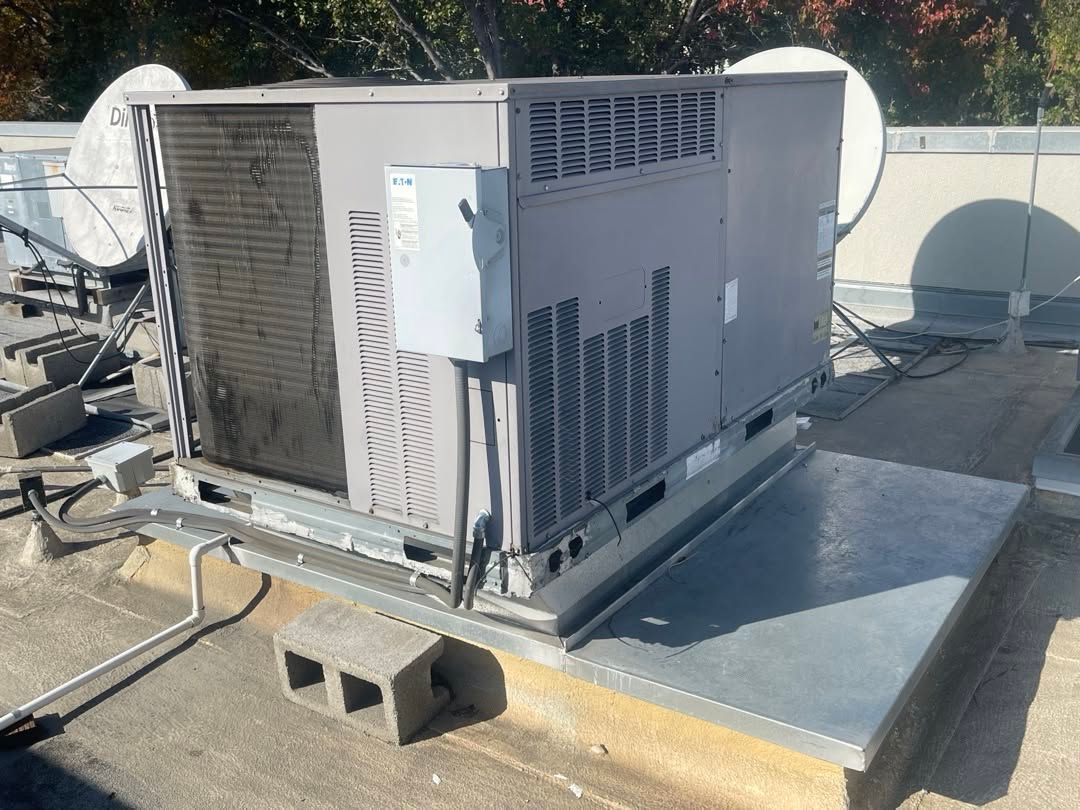 Commercial HVAC unit on a rooftop beside satellite dishes, with a metal platform and cinder blocks.