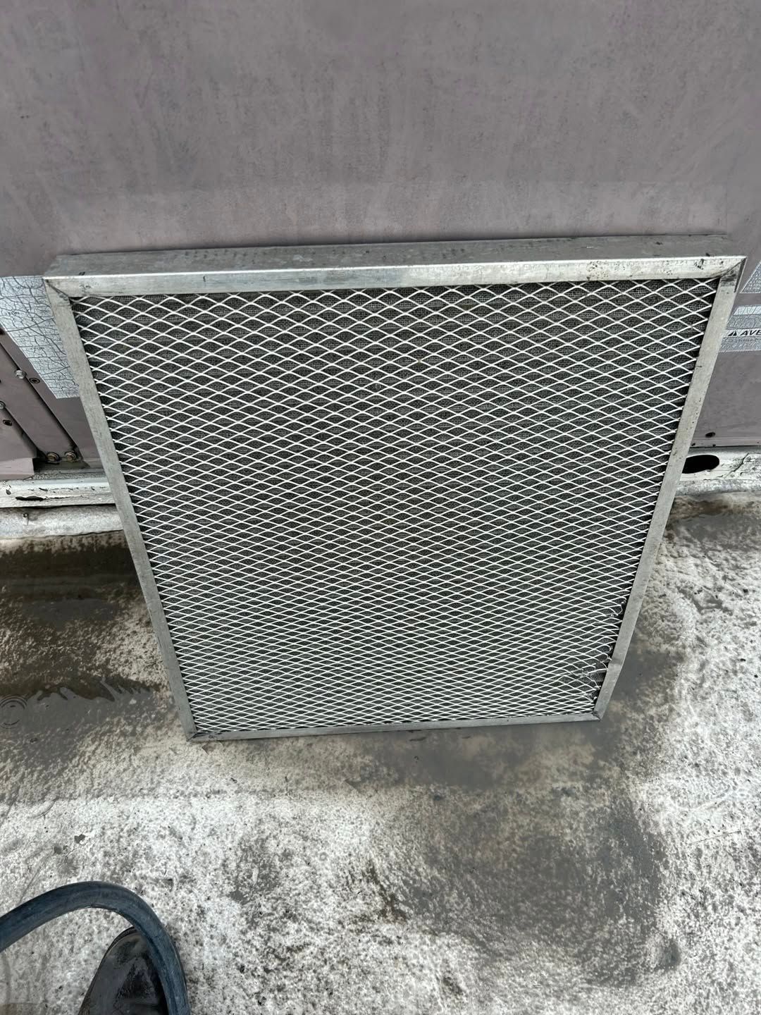 Metal vent cover leaning against a gray wall on a concrete floor