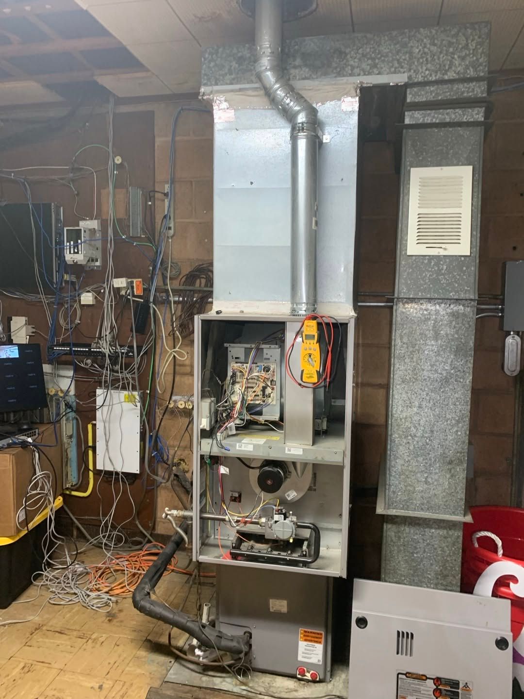 Open furnace unit in basement with exposed wiring and ductwork, maintenance panel removed