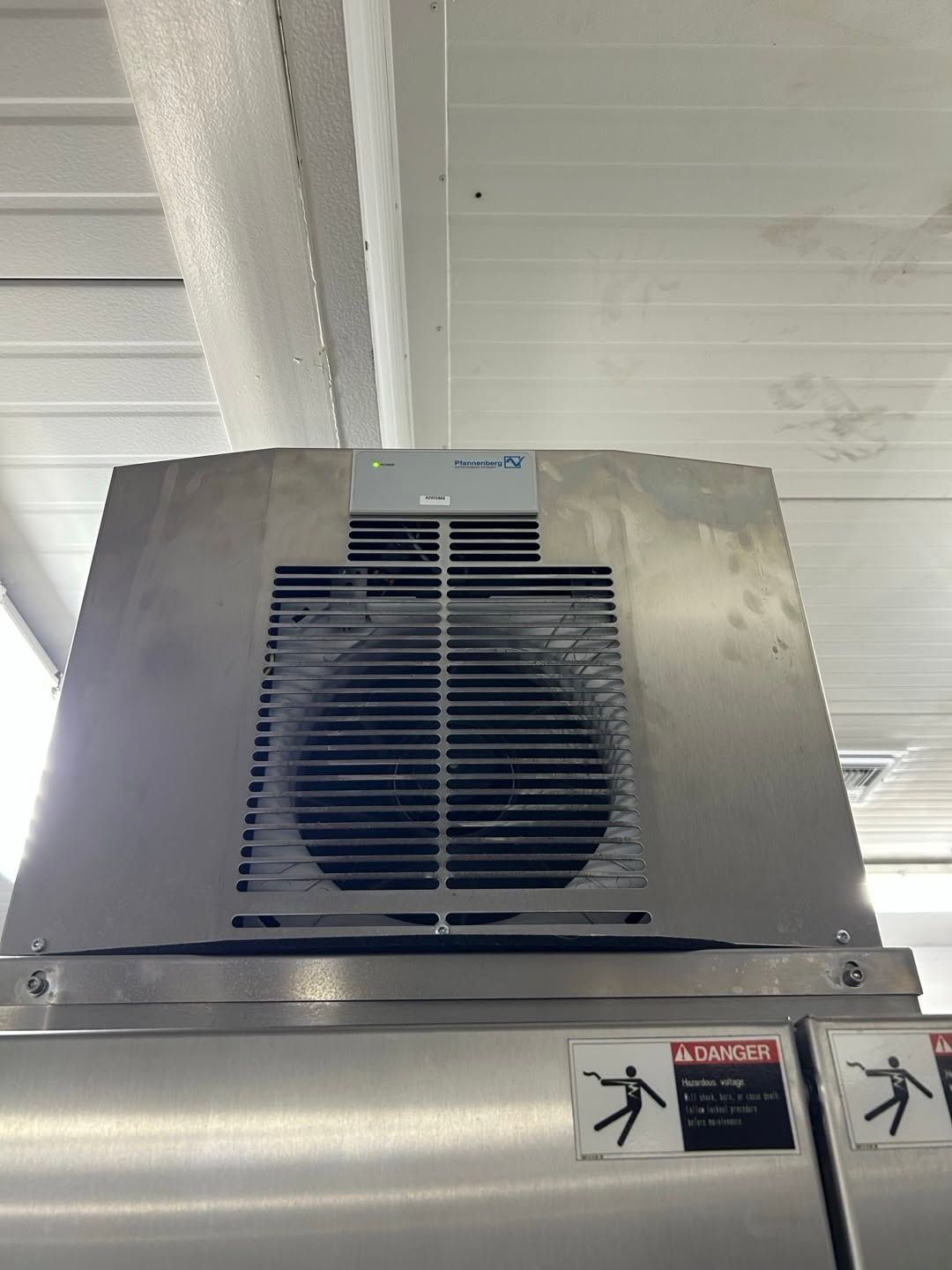 Industrial ventilation unit mounted above a metal surface, with ceiling beams visible in the background.
